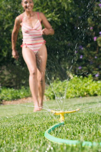 A close-up view of a sprinkler head installed in a grassy area. The sprinkler is positioned upright, surrounded by lush green grass, indicating a well-maintained lawn. The background is blurred, focusing on the sprinkler.