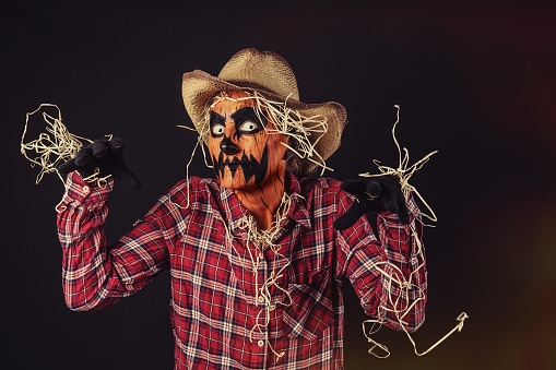 A studio image of a woman with her face painted like a creepy jack o'lantern and dressed as a scarecrow.