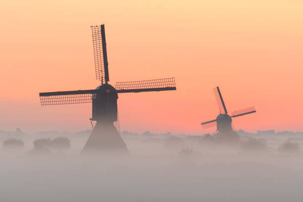 istock 2 windmills in the mist during sunrise. 1035141688