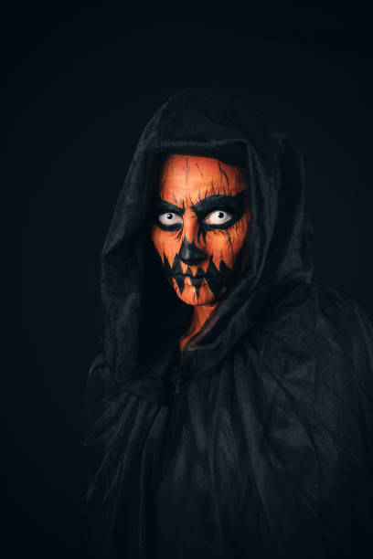 A studio image of a woman with her face painted like a creepy jack o'lantern and staring in a terrifying way at the camera.