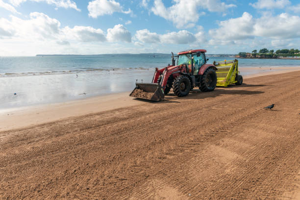 Torquay, UK - September 9, 2018: A man operates a tractor, raking the sand on the beach in Torquay. A popular tourist destination kept clean by the council.