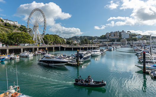 Torquay, UK - September 9, 2018: Four men on a small boat exit the marina where many other boats are moored. The town and ferris wheel in Torquay in the background.