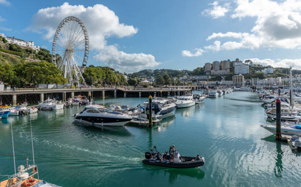 Boats in the marina in Torquay, Devon Torquay, UK - September 9, 2018: Four men on a small boat exit the marina where many other boats are moored. The town and ferris wheel in Torquay in the background. torquay uk stock pictures, royalty-free photos & images