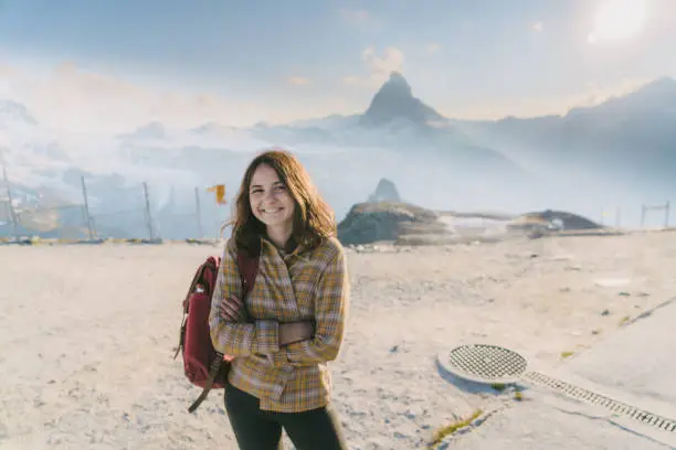 Young Caucasian woman with backpack standing  on the background of scenic  view on  Matterhorn mountain in Switzerland