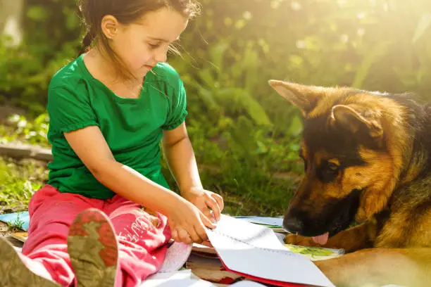 Little girl playing with dog outside, stroking german shepherd lying on porch, leisure of cozy warm happy family in country house