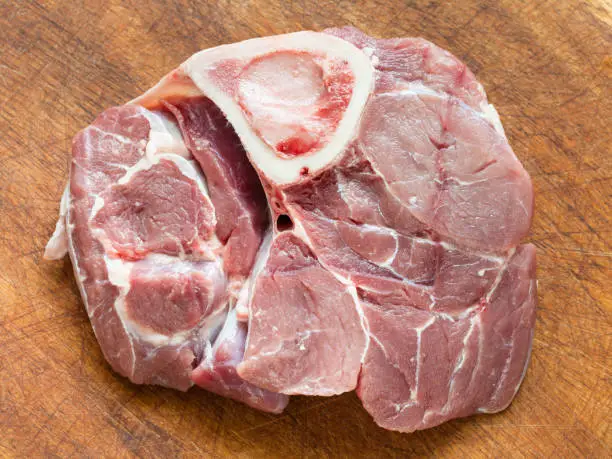 top view of slice of raw veal meat with marrowbone for italian dish Ossobuco on wooden cutting board,