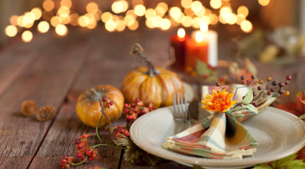 Autumn Thanksgiving dining table place setting on an old wood rustic table Autumn Thanksgiving dining table place setting on an old rustic wood table with candles and defocused Christmas lights beautiful table setting stock pictures, royalty-free photos & images