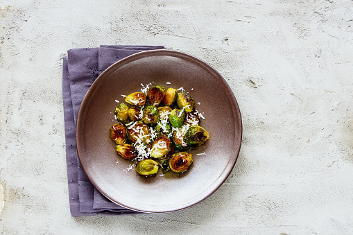 Flat lay of fried Brussels sprouts with parmesan cheese in plate on concrete copy space background. Healthy balanced eating. Top view