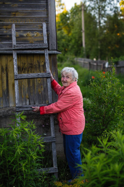 uma mulher idosa fica perto da casa dela aldeia segurando uma escada de madeira. - 15821 - fotografias e filmes do acervo