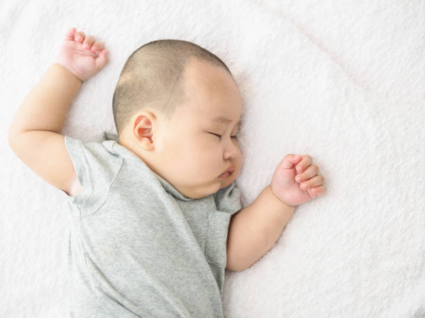 portrait of newborn chinese baby child sleeping in bed after bath or shower. arms raised up and eyes closed. textile and bedding for kids. - baby lying down sleeping asian ethnicity imagens e fotografias de stock