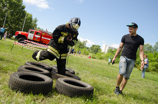 Komsomolsk-on-Amur, Russia - August 8, 2016. Public open Railroader's day. girl in the uniform of fireman jumps on obstacles course of tires