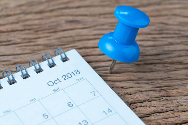 istock October 2018 calendar appointment, deadline, holiday or date planning concept, big blue pushpin or thumbtack pin on wooden table next to Sep white clean calendar 1035291414