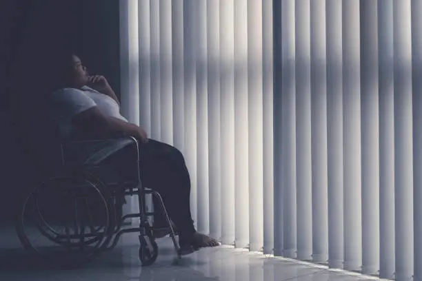Side view of obese woman looks pensive while sitting in the wheelchair by the window. Shot in the hospital