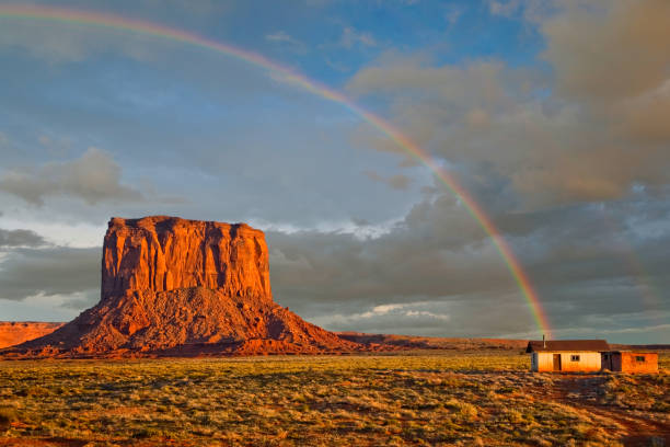 Shack at the End of a Rainbow Monument Valley, on the Arizona - Utah border, gives us some of the most iconic and enduring images of the American Southwest. The harsh empty desert is punctuated by many colorful sandstone rock formations. It can be a photographer's dream to capture the ever-changing play of light on the buttes and mesas. Even to the first-time visitor, Monument Valley will probably seem very familiar. This rugged landscape has achieved fame in the movies, advertising and brochures. It has been filmed and photographed countless times over the years. If a movie producer was looking for a landscape that epitomizes the Old West, a better location could not be found. This picture of Mitchell Butte with a shack at the end of a rainbow was photographed from the Monument Valley Road north of Kayenta, Arizona, USA. jeff goulden monument valley stock pictures, royalty-free photos & images