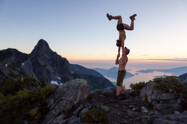 Acro Yoga on top of a Mountain Man and Woman doing acroyoga on top of a mountain during a vibrant summer sunset. Taken in Howe Sound, near Vancouver, BC, Canada. acroyoga stock pictures, royalty-free photos & images