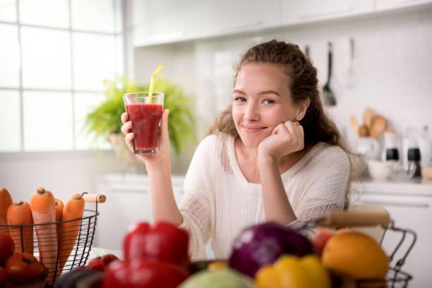 mulher jovem e saudável em uma cozinha com frutas e legumes e suco - dieting juice carrot tomato - fotografias e filmes do acervo