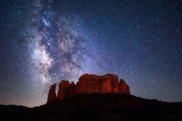 A bright green meteor streaks through the Milky Way and starry night sky above Cathedral Rock in Sedona, Arizona.