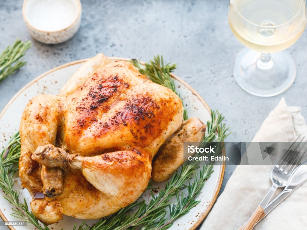 Pollo alla griglia intero con pelle caramellata e rosmarino fresco su un tavolo da pranzo. - Foto stock royalty-free di Pollame - Uccello