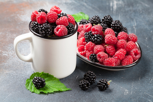 Cup of ripe blackberries and raspberries on stone table
