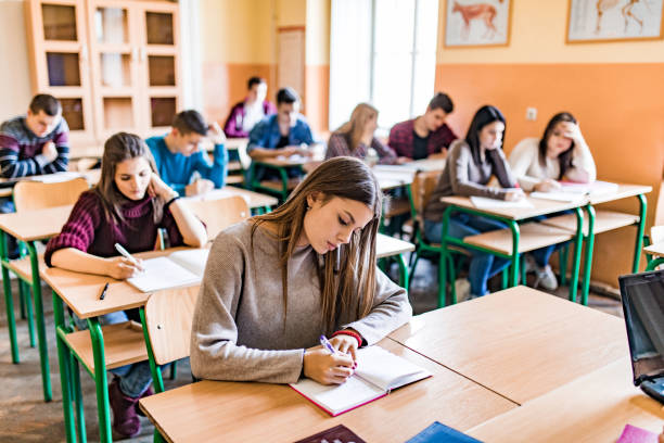 Group of high school students writing a test in the classroom. Large group of students sitting in the classroom and writing a test. high school building stock pictures, royalty-free photos & images