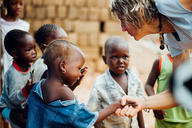 White caucasian mature woman shaking hands with black african people in a rural village Mali, Africa - circa August 2009 - White caucasian mature woman shaking hands with black african boys in a rural village near Bamako africa volunteer stock pictures, royalty-free photos & images