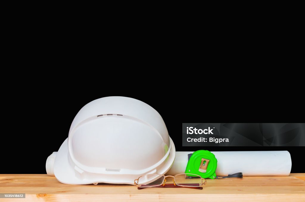 helmet plastic white with glasses, paper roll plan blueprint and measuring tape green. hat safety equipment working of engineering concept construction on Wooden floor isolated black background clipping path Engineer Stock Photo