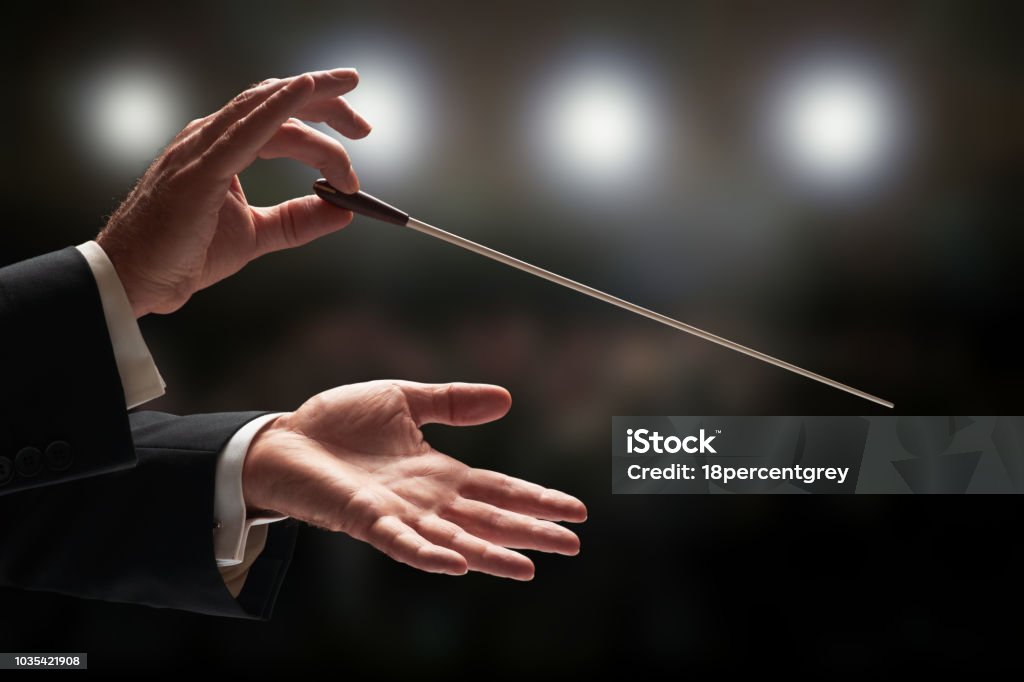 Conductor conducting an orchestra Conductor conducting an orchestra with audience in background Musical Conductor Stock Photo