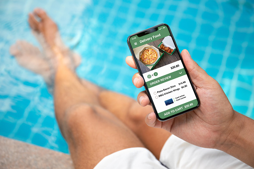 man holding phone with app delivery sushi food on screen by the pool