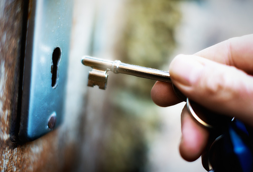 A hand holds a key on  a key ring, about to lock or unlock an old wooden door.