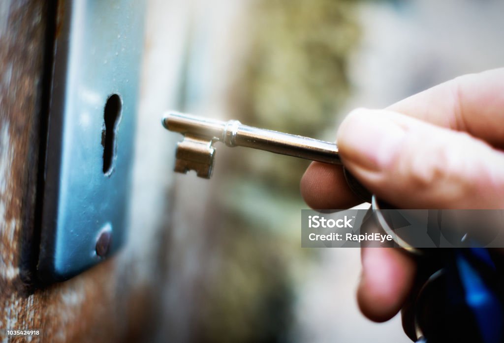 Hand holding key to unlock  battered old wooden door A hand holds a key on  a key ring, about to lock or unlock an old wooden door. Key Stock Photo