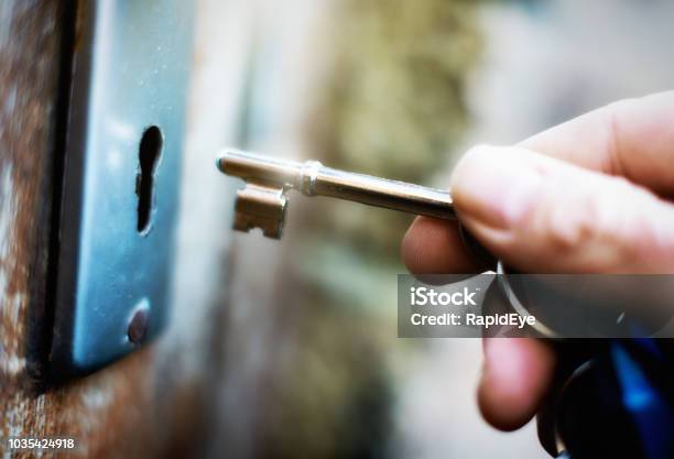 Hand Holding Key To Unlock Battered Old Wooden Door Stock Photo - Download Image Now