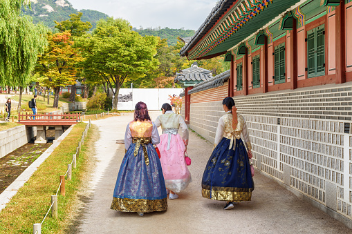 Seoul, South Korea - October 9, 2017: Girls wearing Korean traditional dress Hanbok in Gyeongbokgung Palace. Young women walking in royal garden. Beautiful autumn cityscape.