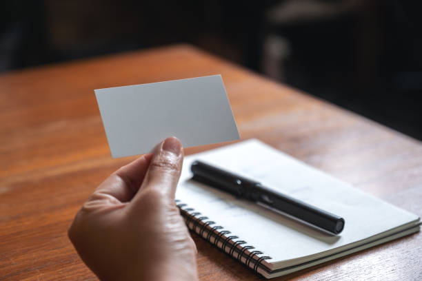 istock A hand holding white empty business card with notebook on wooden table 1035452072