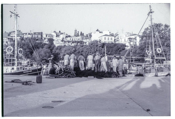 1989 black and white shot of Greek fishermen sorting out fishing nets in the harbour of Skiathos, Greece