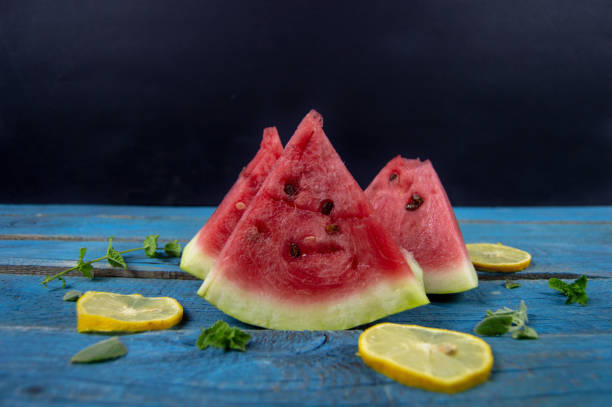 pieces of ripe watermelon, lemon, grapes and mint on a blue and black background stock photo