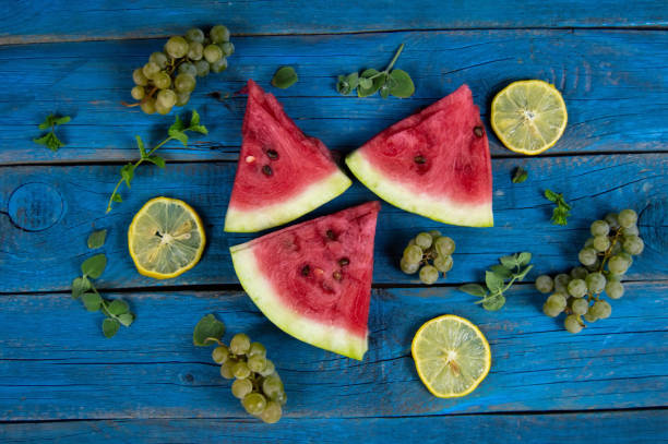 pieces of ripe watermelon, lemon, grapes and mint on the background of a blue wooden table stock photo