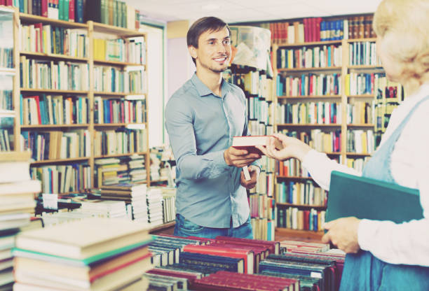 istock Young smiling man taking chosen book from seller 1035488366