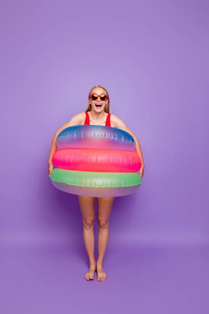 夏の準備を!楽しいの概念は、ビーチで休暇します。紫色の背景に分離されて腰にカラフルな浮き輪を持つ女の子の全身肖像画 - celebration inflatable excitement concepts ストックフォトと画像