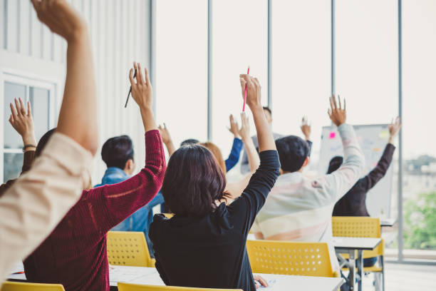 gruppo di uomini d'affari alzano la mano per concordare con il relatore nel seminario della sala riunioni - cheering arms raised women university foto e immagini stock