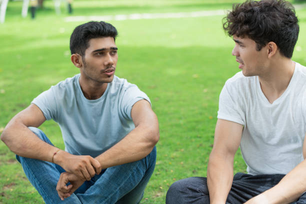 Serious Indian guy sharing problem with friend in summer park Serious Indian guy sharing problem with friend in summer park. Handsome young men sitting on grass and talking. Chatting concept indian man walking in park stock pictures, royalty-free photos & images