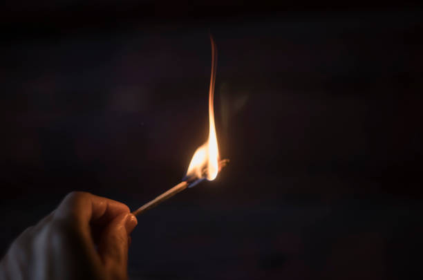 Burning match in the hand at firewood background