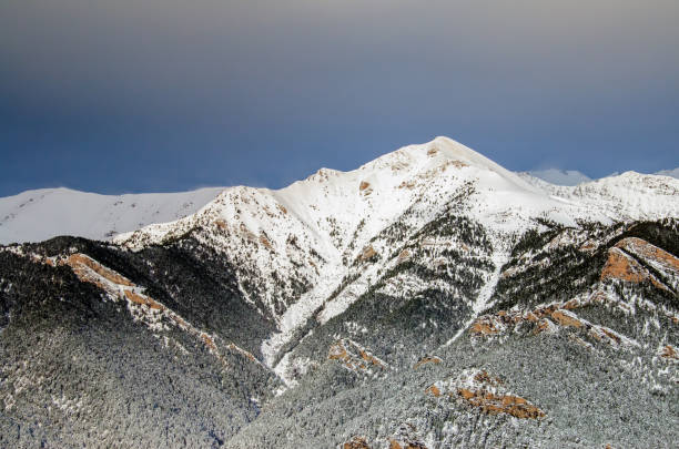 Winter themed landscape with Andorra's snowcapped mountain range, blue sky and forest under snow. Strong wind blows the snow off the top of mountains. Background with copy space.