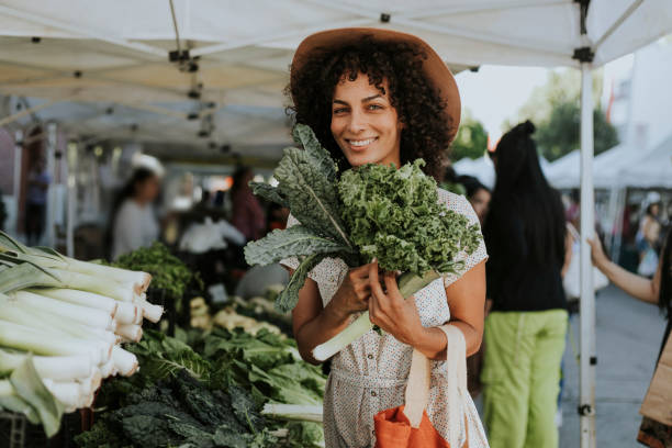 hermosa mujer compra kale en un mercado - comida vegana fotos fotografías e imágenes de stock
