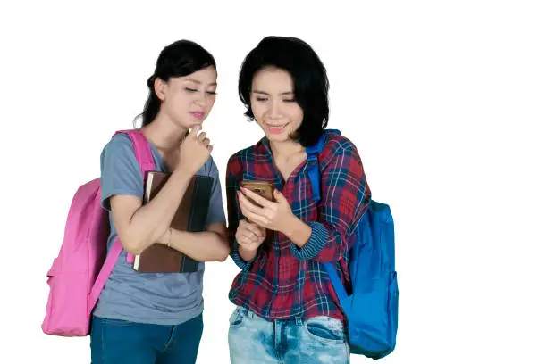 Picture of two female college students using a smartphone together, isolated on white background