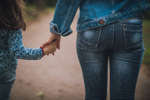 Two women, young mother and little daughter, relaxing in park on a lovely day, holding hands.