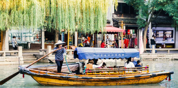 Suzhou, China - Nov 5, 2016: Boat with tourists cruising by at the historic Zhouzhuang Water Town. Other visitors activities can be seen on the shoreline.