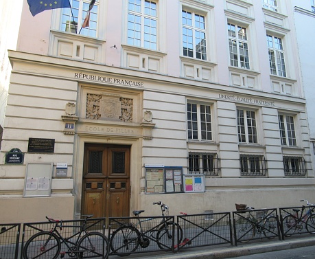 Facade of a traditional French School for girls in Paris with bikes parked along the sidewalk. A panel next to the front door reads that this school participated in the 1943-1944 deportation of Jewish children to the German death camps.