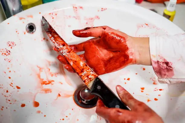 Halloween horror concept. Closeup of unknown woman hands holding a bloody knife in the sink