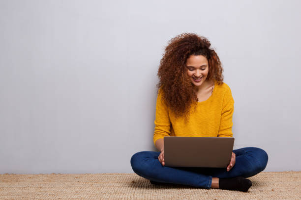 mujer joven feliz sentada en suelo con ordenador portátil - sentado en el suelo fotografías e imágenes de stock