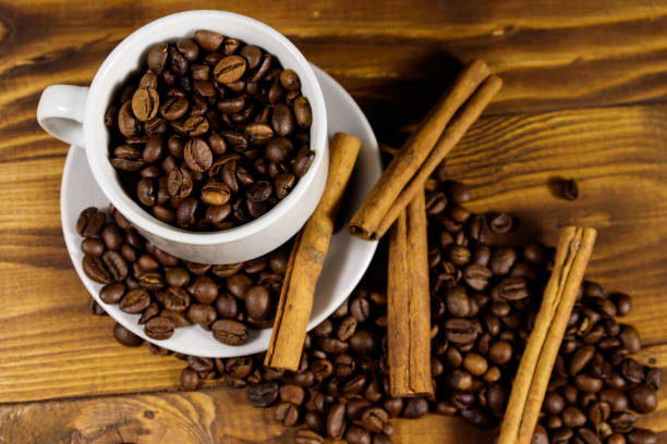 istock Coffee beans in white cup and cinnamon sticks on wooden table. Top view 1035625682